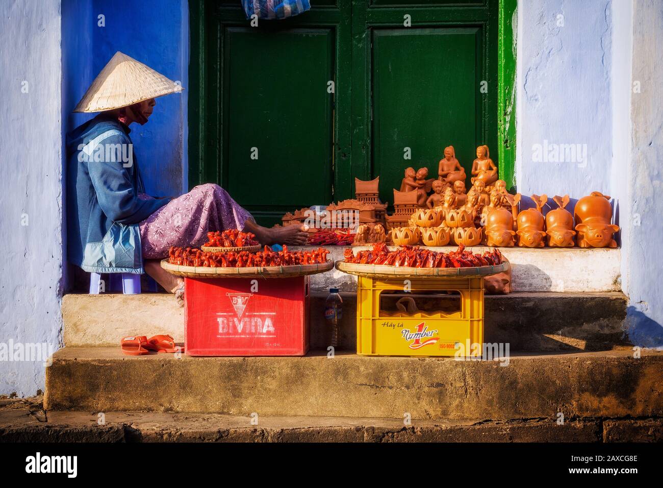Vietnamese street vendor wearing traditional straw hat selling handicrafts on the street in Hoi An Ancient Town, Central Vietnam. Stock Photo