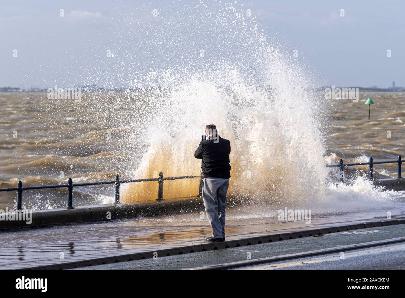 Lone male using mobile phone to photograph a crashing wave coming towards him on Western Esplanade, Southend on Sea, Essex, UK. Camera phone. Ciara Stock Photo