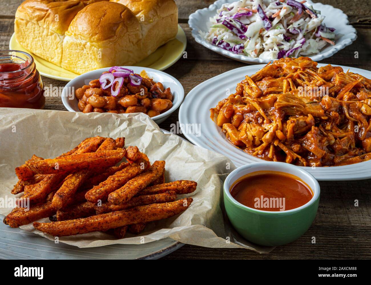 Vegan BBQ plate. Jack-fruit barbecued, Southern style baked beans, coleslaw, dinner rolls and sweet potato fries. Stock Photo