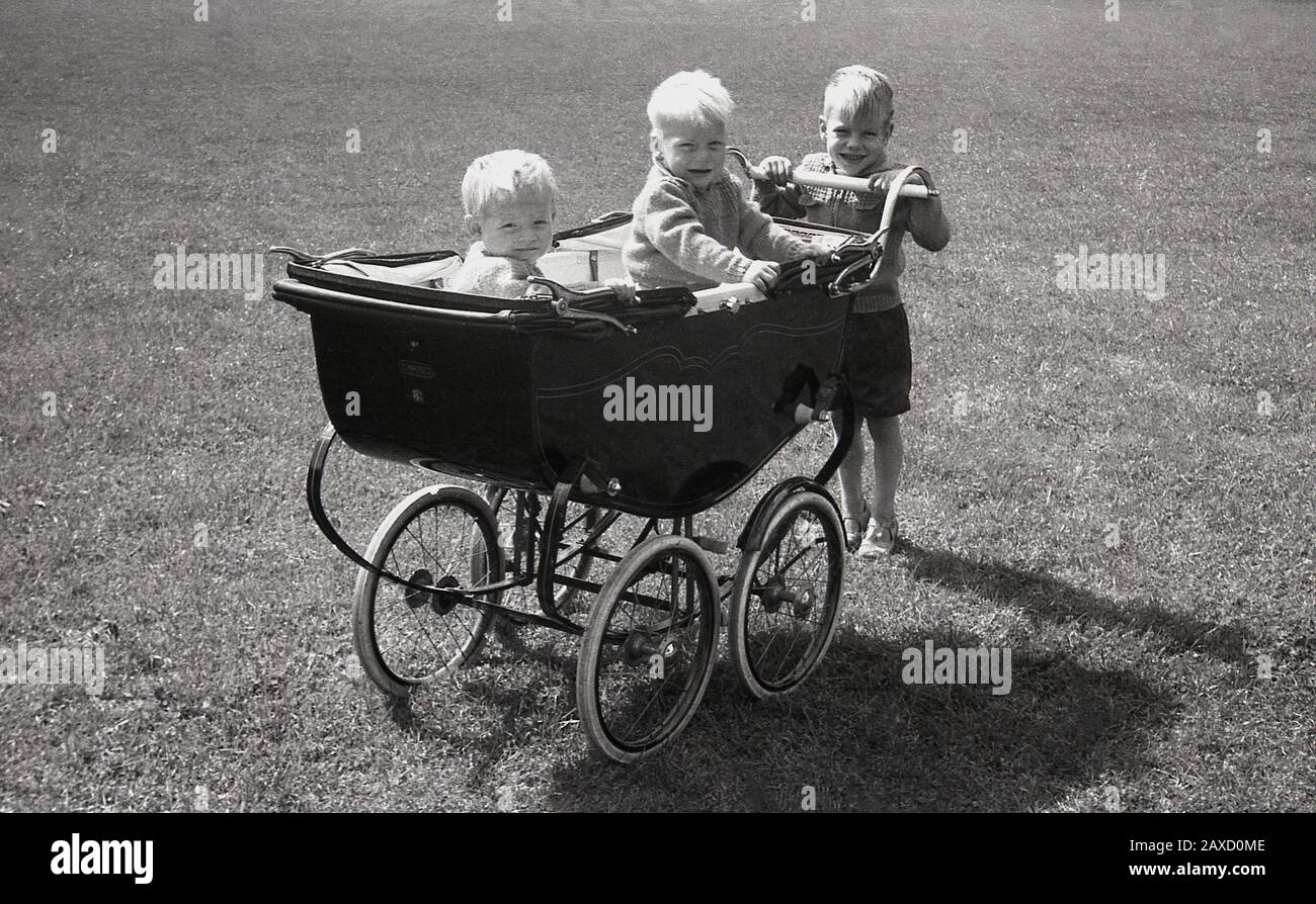 1940s, historical, three infant boys, one holding the handle and two sitting inside in a luxury Briitsh made 'Harris' coach-built baby carriage sat in a park, England, UK. Founded in 1870 in the Old Kent Rd, London, by William James Harris as a reseller of sewing machines - Harris had worked for the Singer Sewing Company for several years - in 1880 Harris decided to begin make his own prams, which became their main business activity. The company was brought by Mothercare in the 1960s. Stock Photo