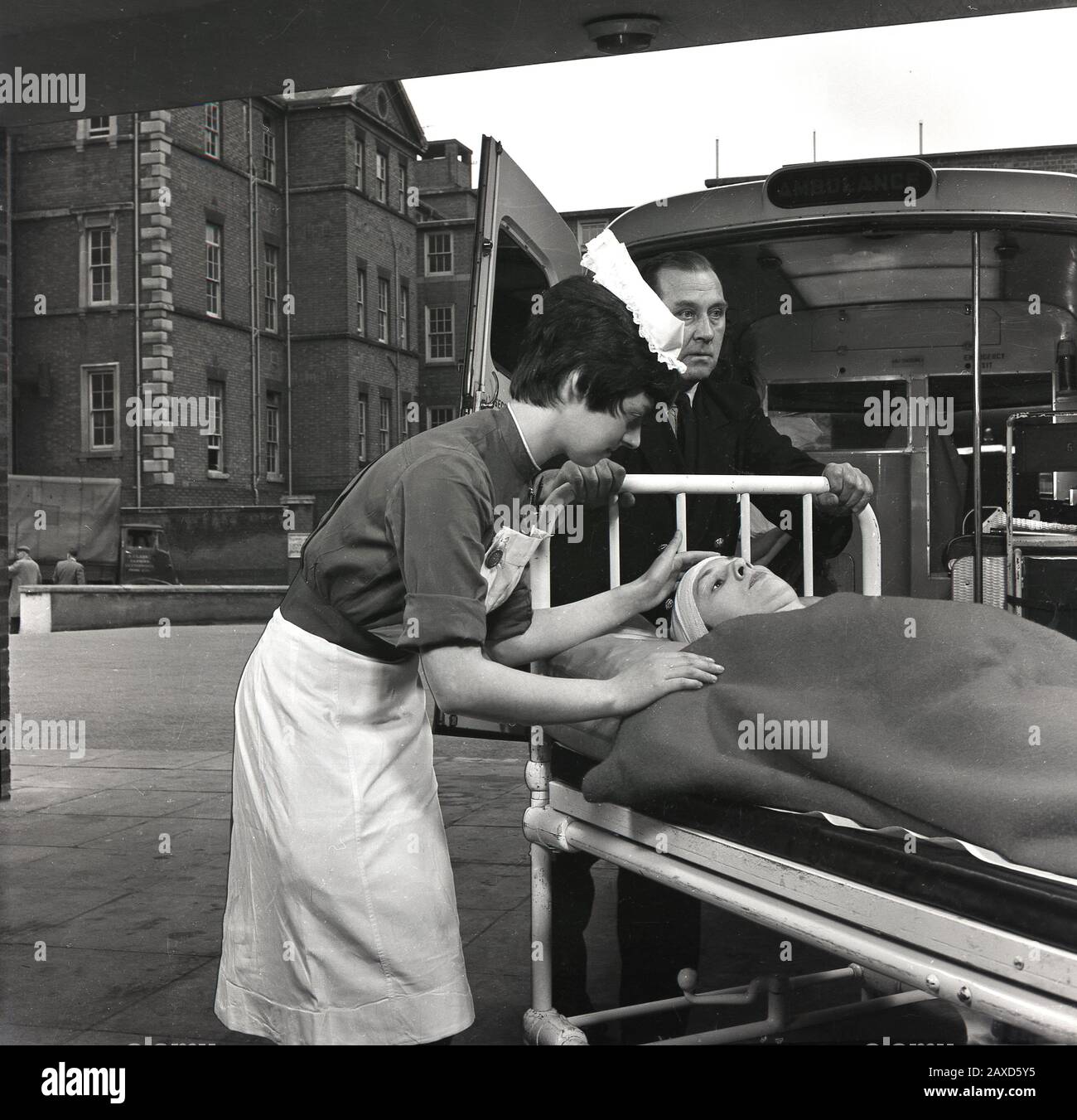 1960s, historical, outside a hospital, a young nurse comforting a patient on a trolly bed with a head injury, as she is taken from an aumbulance, South London, England, UK. Stock Photo