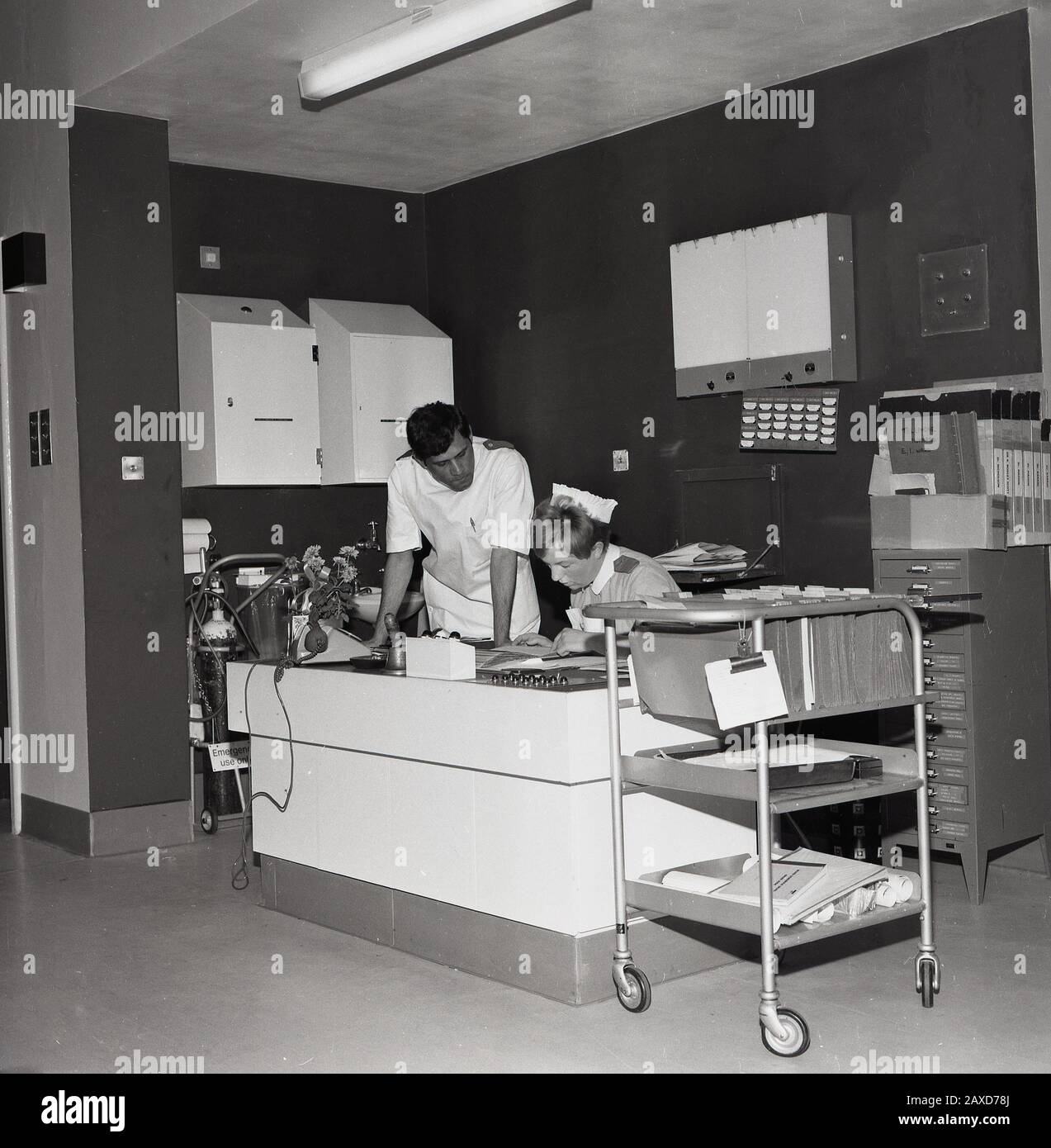 1960s, historical, two nurses at a front desk of a ward, the female nurse looking through medical notes at Brook General hospital, South London, England, UK. Stock Photo