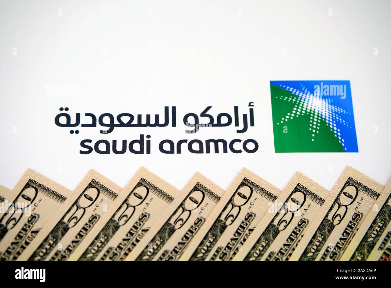 Saudi Aramco logo and stack of dollar banknotes. Saudi Arabian Oil Company is one of the largest companies in the world by revenue. Stock Photo