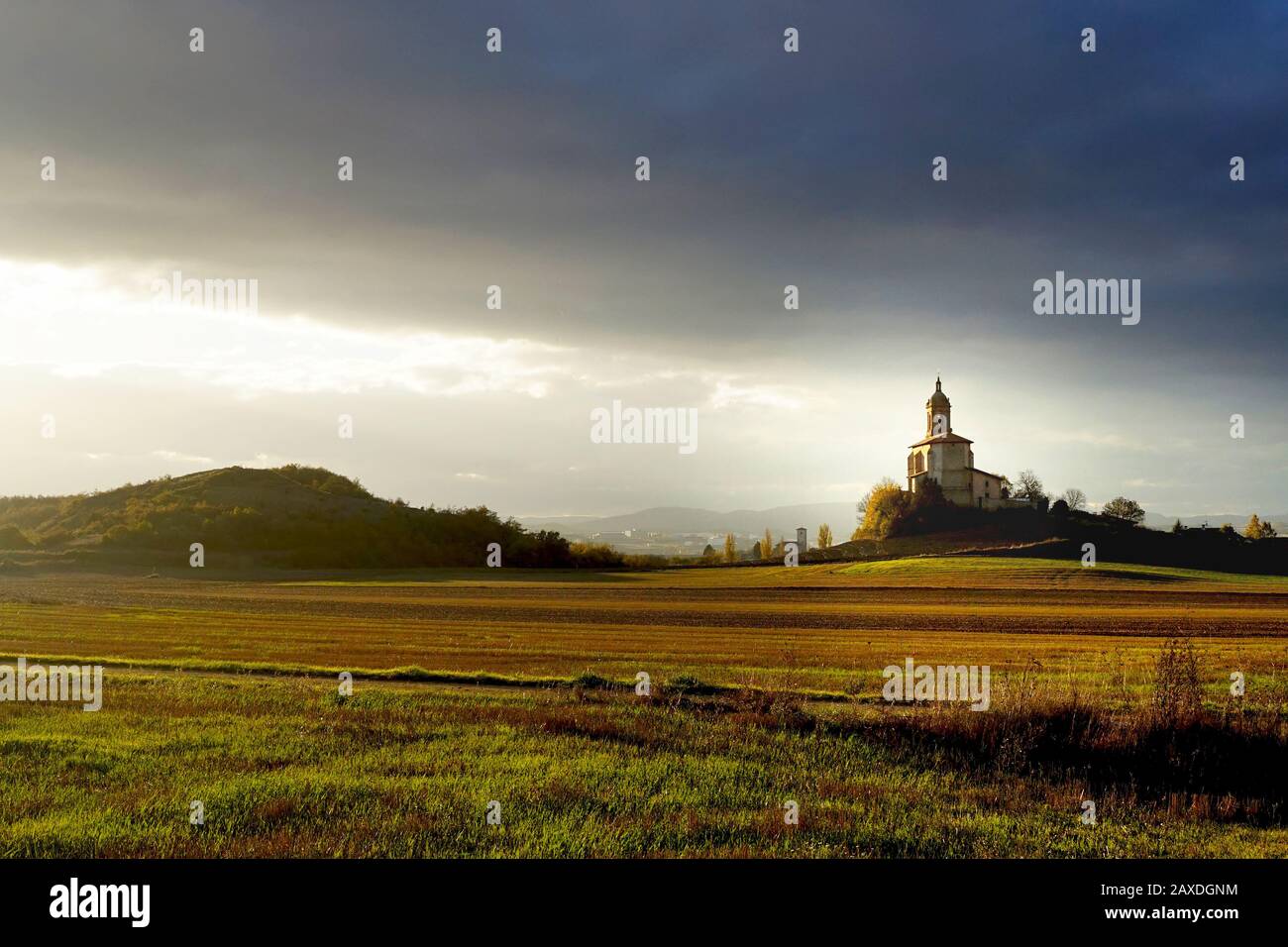 Dark skies over an old Church stood alone on a hill bathed in sunlight Stock Photo