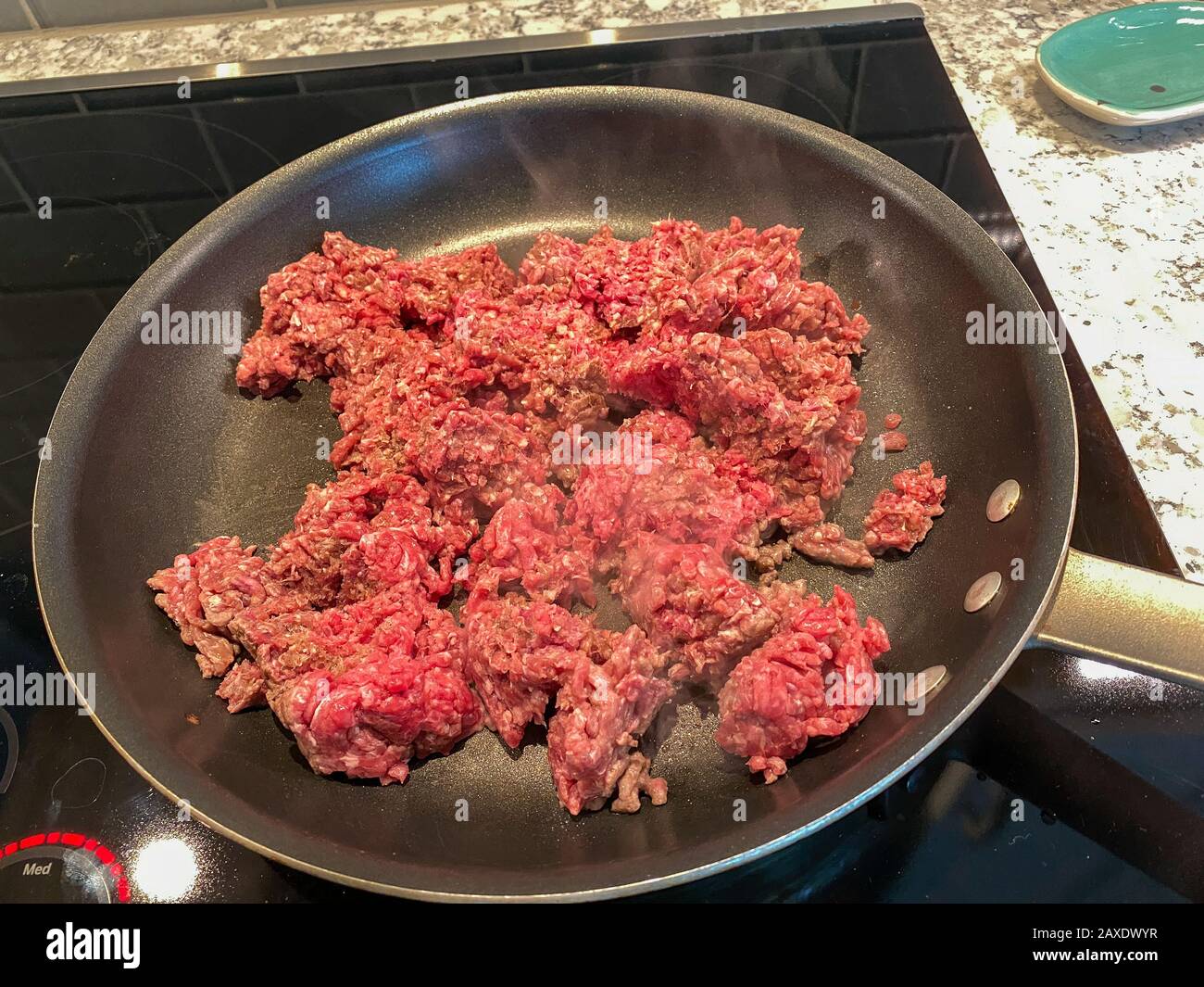 A pan of sizzling ground beef cooking on a stove with smoke coming off