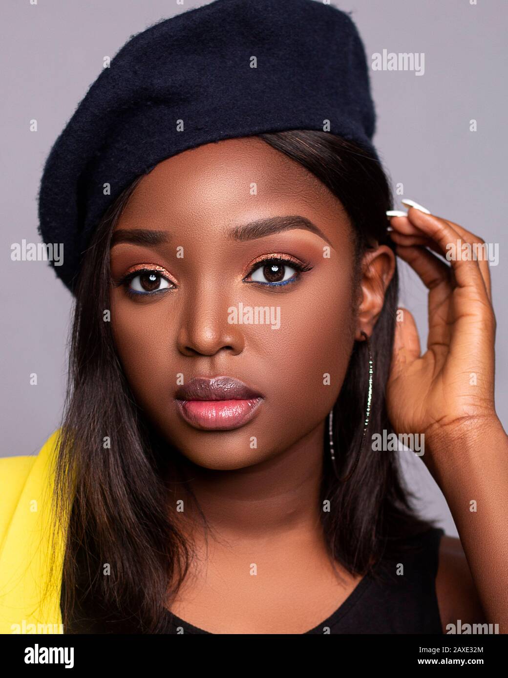 Close up portrait of young beautiful African lady on a grey background with a hat with beautiful skin and eyes Stock Photo