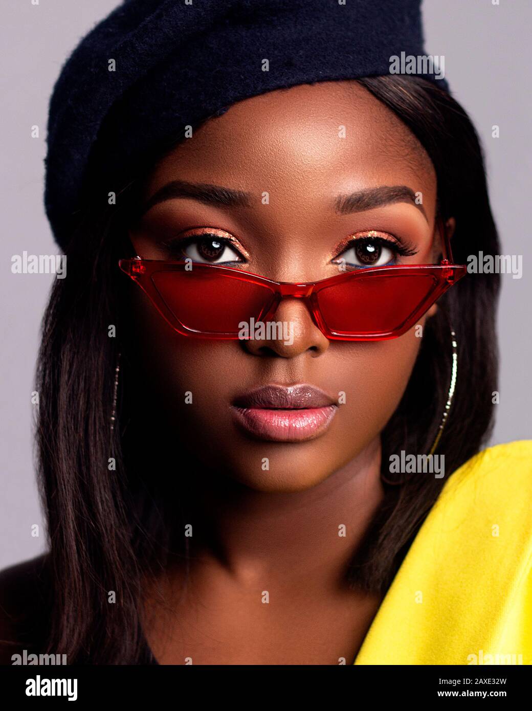 Close up portrait of young beautiful African lady wearing glasses on a grey background with a hat Stock Photo