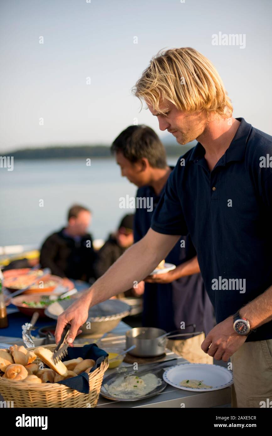 Young blond man helping himself to lunch at a waterfront location Stock Photo