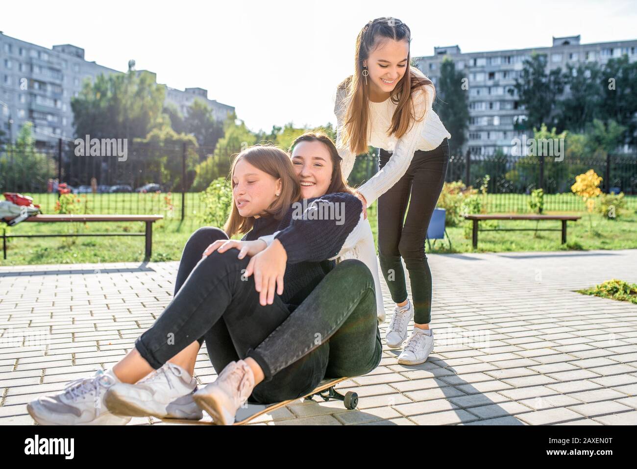Three teenage girls of 12-14 years old, in summer in city, ride a skateboard, happy smiling, having fun and rejoicing. Weekend break. Casual clothes Stock Photo