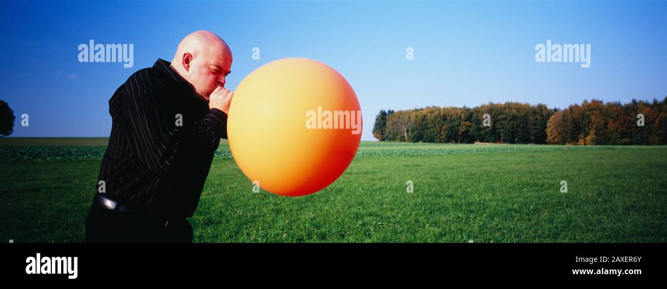 Side profile of a mature man blowing a balloon, Germany Stock Photo
