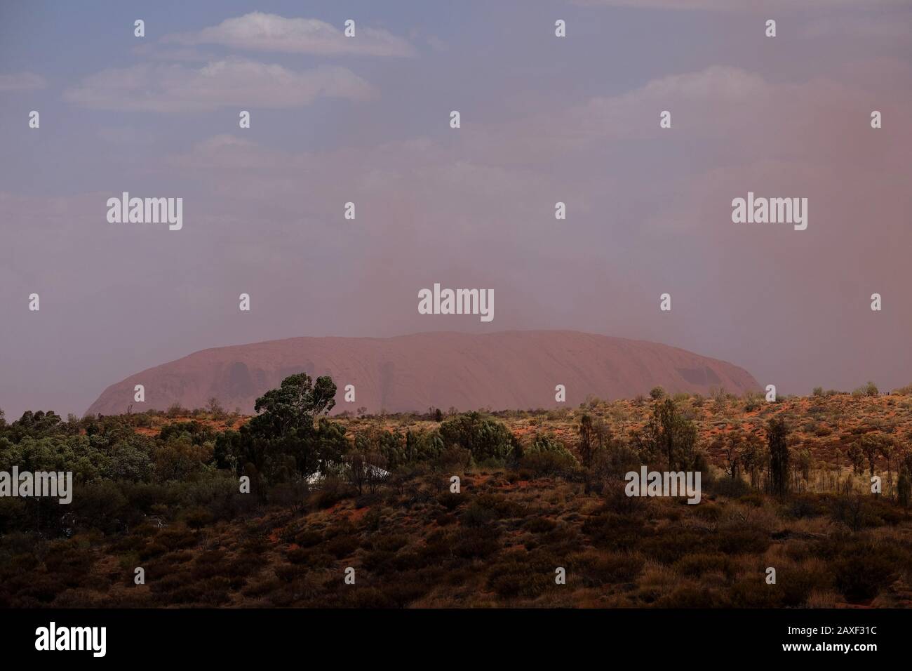 A cloud of red dust storm passes in front of Uluru, the massive sandstone monolith in the Northern Territory’s 'Red Centre' arid desert region Stock Photo