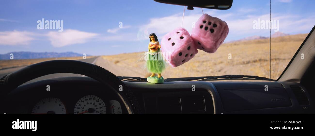 Fuzzy dices hanged on a rear view mirror with a hula girl figurine on the dashboard of a car Stock Photo