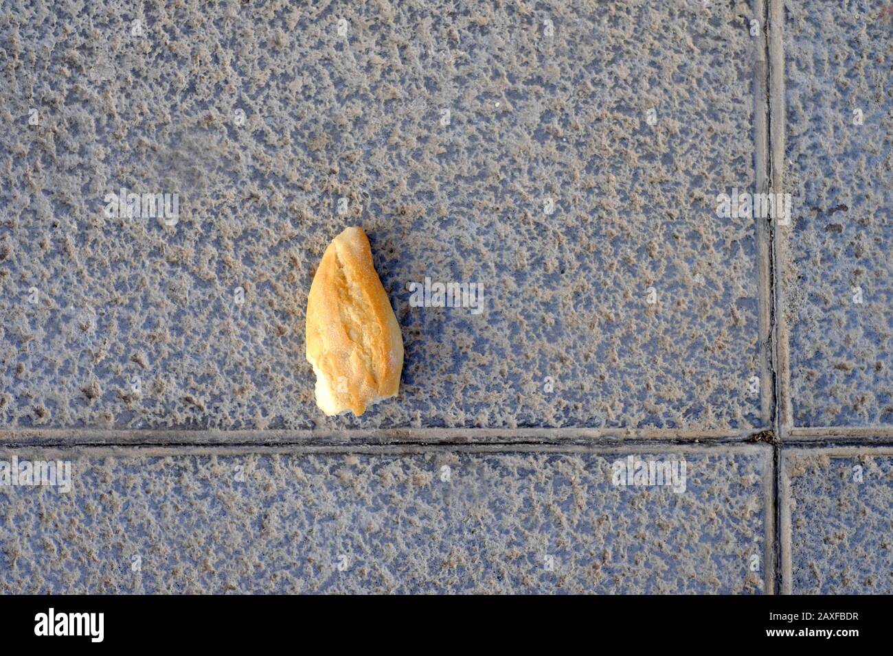 A piece of bread on the ground, food oversupply and food waste. Stock Photo