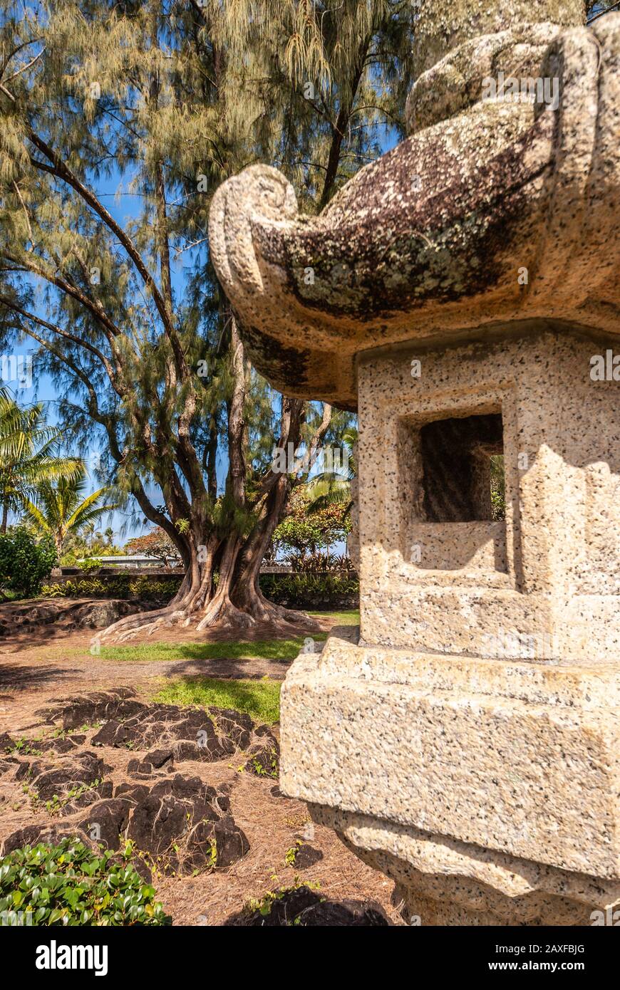Hilo, Hawaii, USA. - January 9, 2012: Part of beige stone Japanese lantern and brown dirt, black lava stone and green trees in Liliuokalani Gardens. B Stock Photo