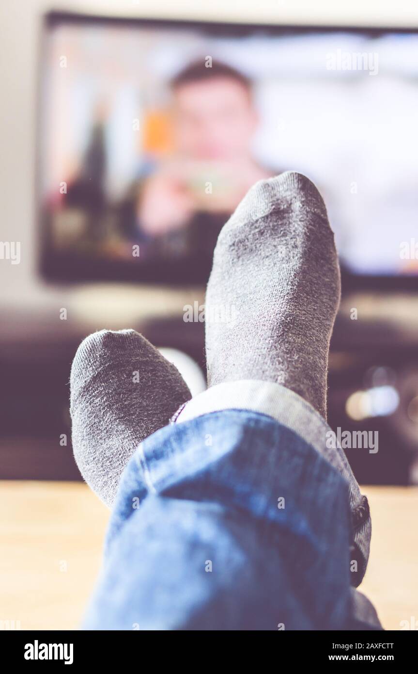 Vertical picture of crossed feet under the lights with the tv on the blurry background Stock Photo