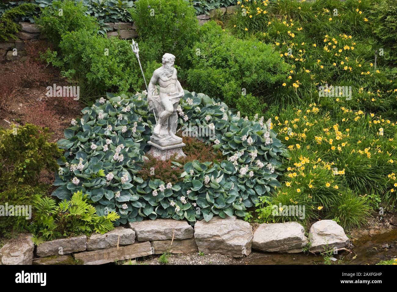 Sculpture of Neptune surrounded by Hosta plants, yellow Hemerocallis - Daylily flowers in Five Senses Garden in La Seigneurie de L'Ile d'Orleans, Que Stock Photo
