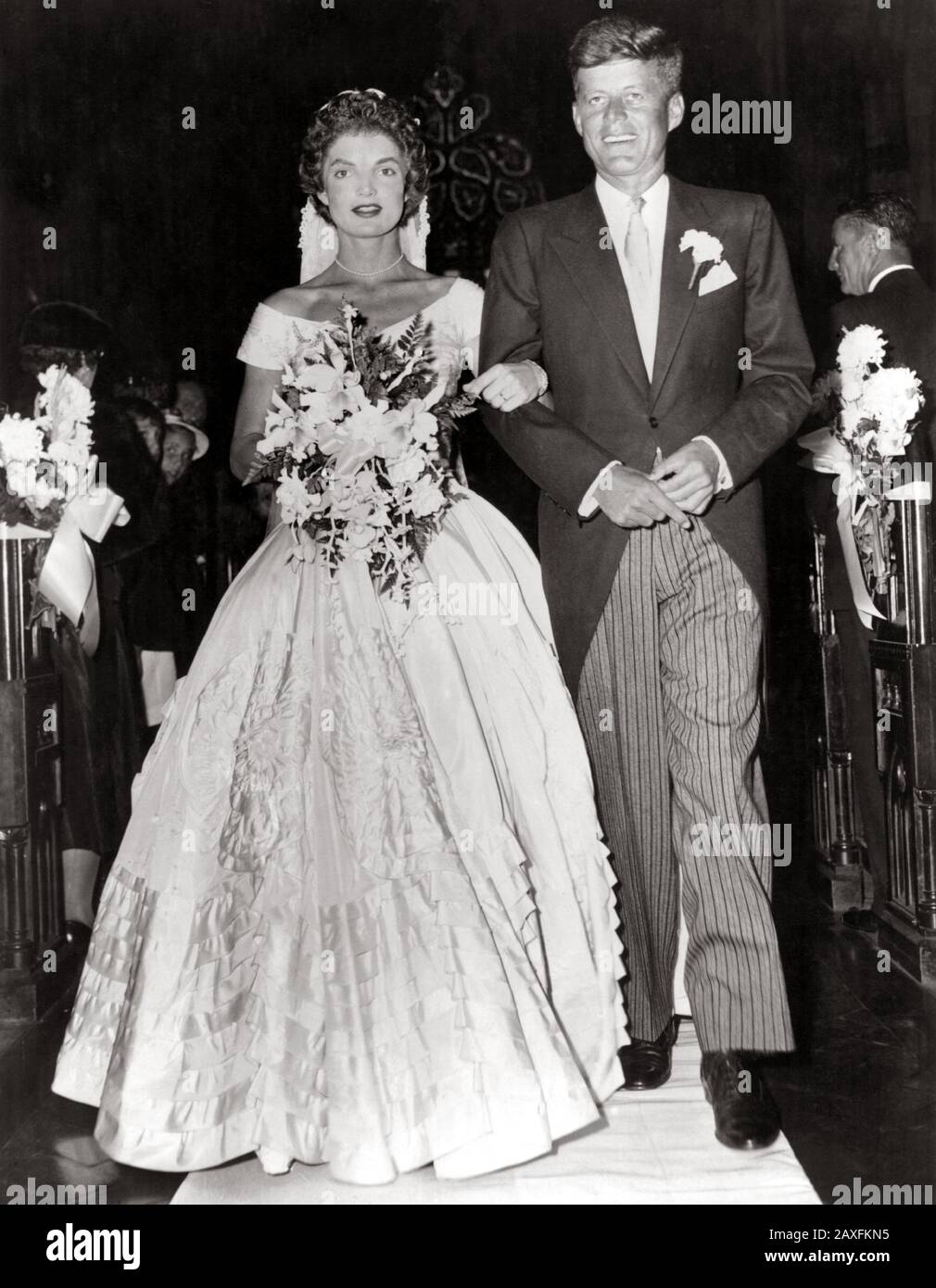1953 , 12 september , Newport, Rhode Island, USA : The future american President JOHN Fitzgerald KENNEDY ( 1917 - 1963 ), Democratic senator for Massachusetts , escorts his bride Jacqueline Lee Bouvier ( 1929 - 1994 ) down the church after their wedding ceremony  - PRESIDENTE DEGLI STATI UNITI D' AMERICA - cravatta  - tie - CASA BIANCA - WHITE HOUSE - POLITICO - POLITIC - POLITICIAN - POLITICA  - sposalizio - matrimonio - WEDDING DRESS - MARRIAGE - SPOSI - MARITO E MOGLIE - bouquet - flowers - fiori - garofano - canation - pochette - fazzoletto nel taschino - abito da sposa - bridal dress - Stock Photo