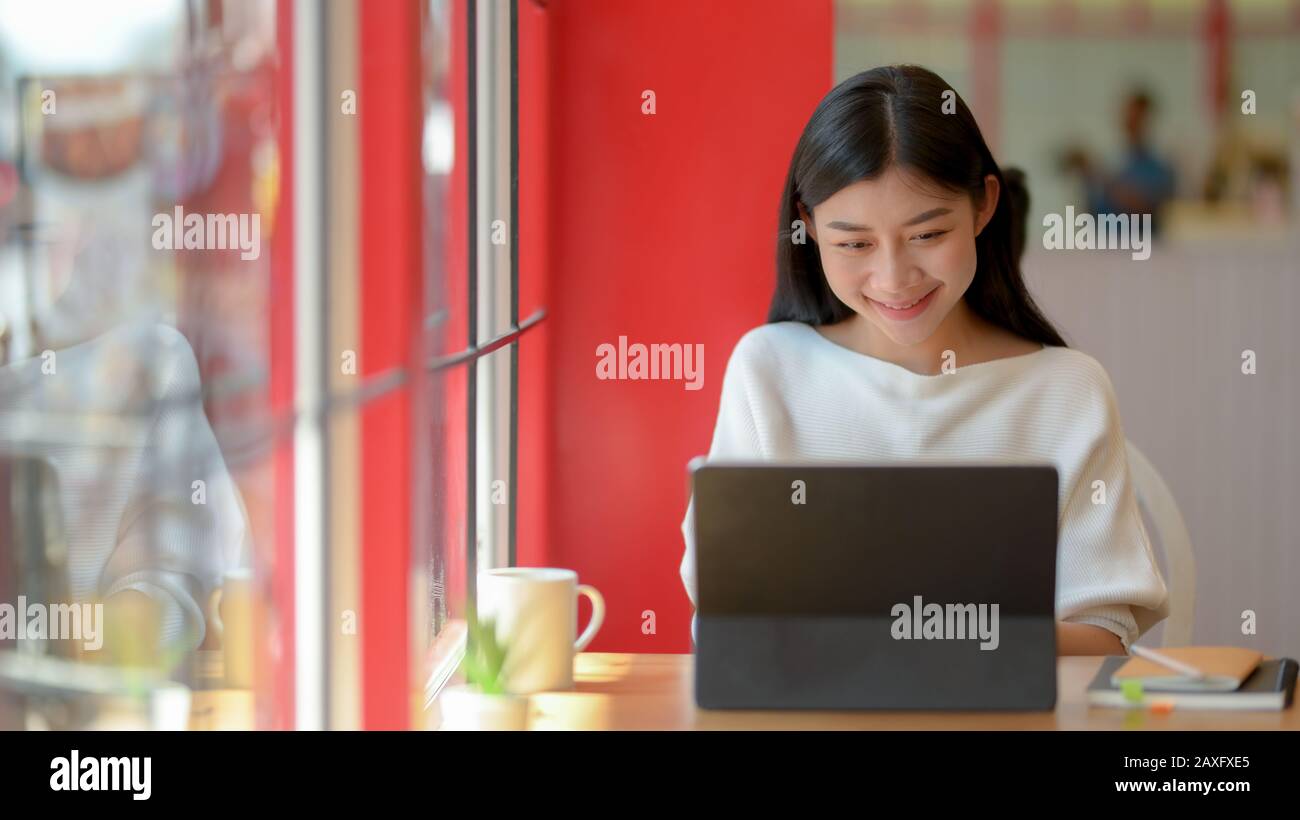 Portrait of adorable college girl working on her assignment with tablet ...