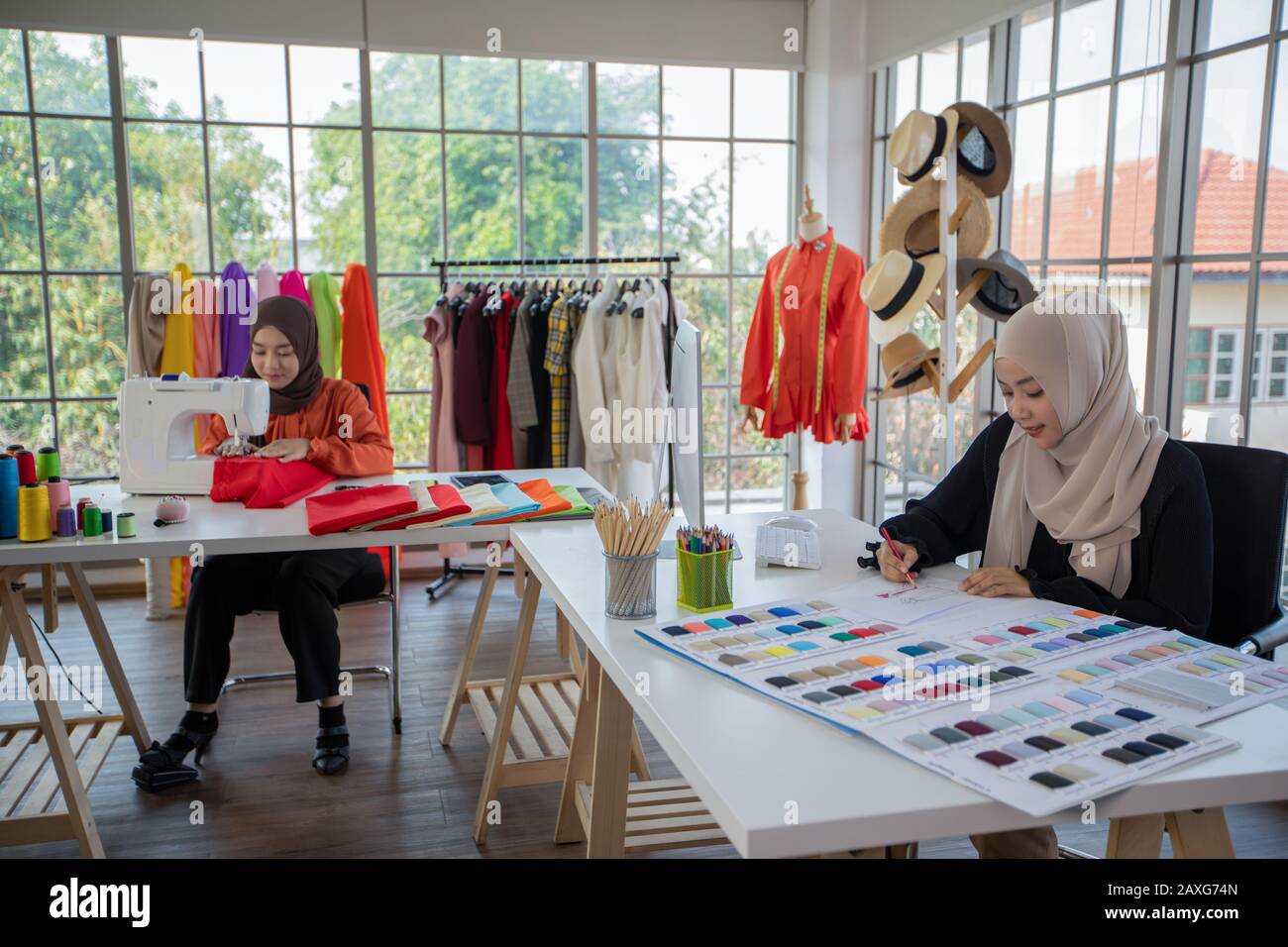 Small business of Muslim woman fashion designer Working and using smart phone and tablet With Dresses at clothing store Stock Photo