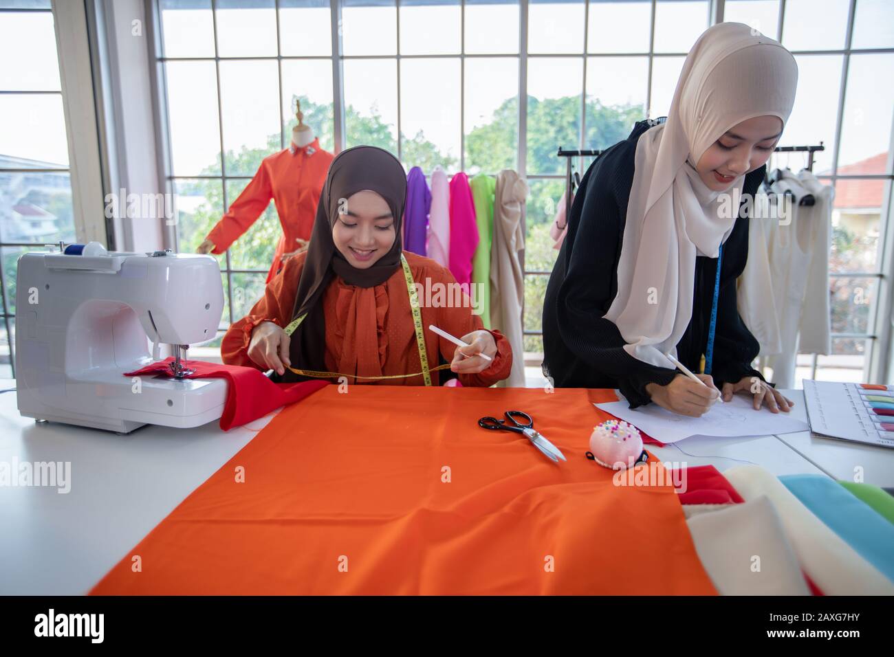 Small business of Muslim woman fashion designer Working and  using smart phone and tablet With Dresses at clothing store Stock Photo