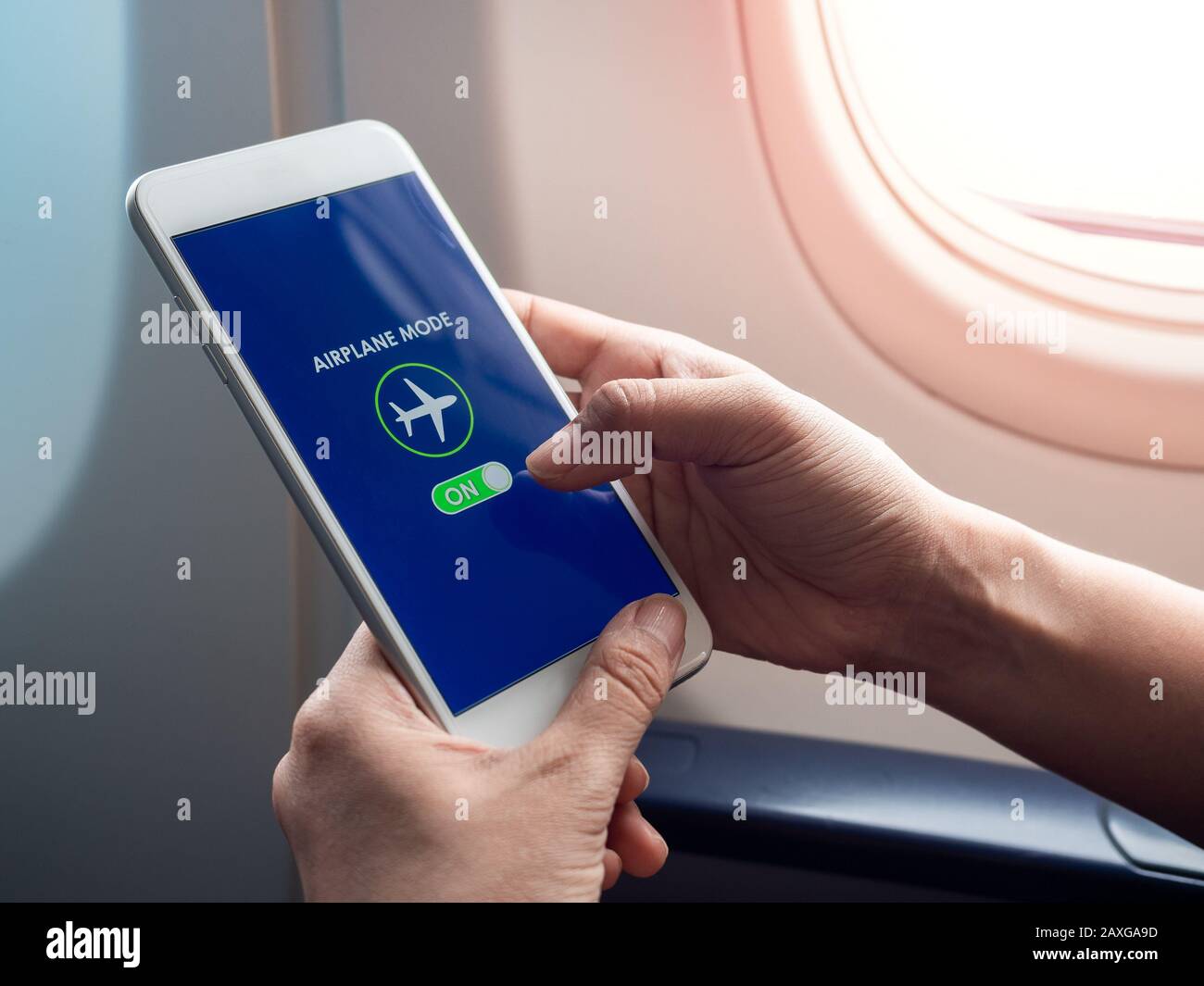 Flight mode concept. Finger sliding on screen for turned on airplane mode near the window on the airplane. Stock Photo
