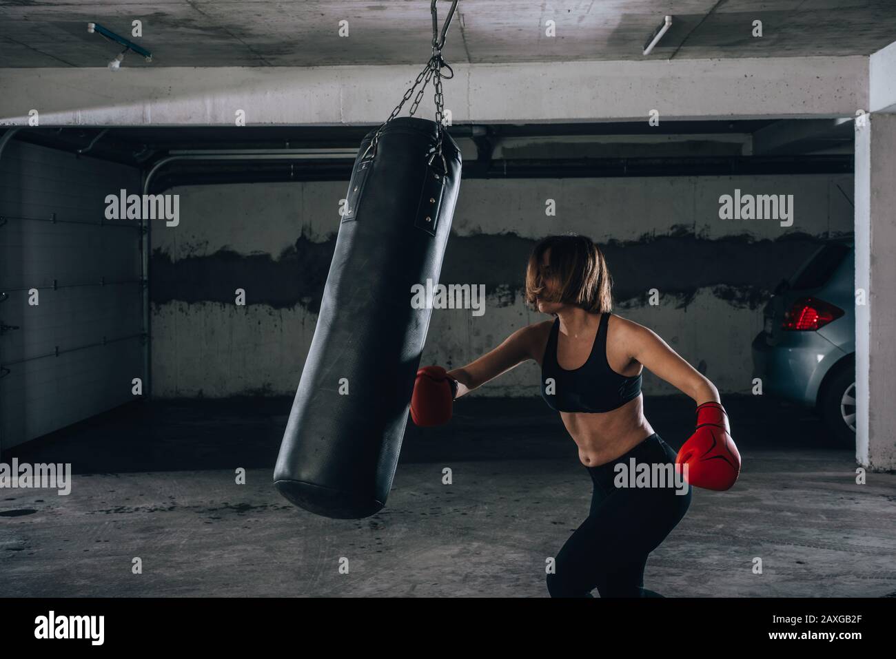 Profile view of a strong young woman punching a boxing bag inside the