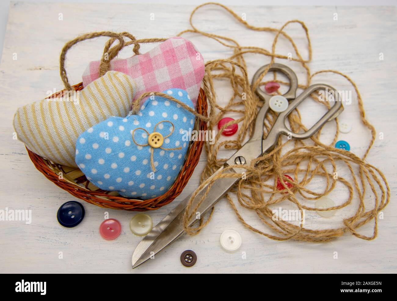 A basket filled with hearts sewn from scraps of fabric, next to large retro tailor's scissors, coarse thread and colorful buttons. Stock Photo