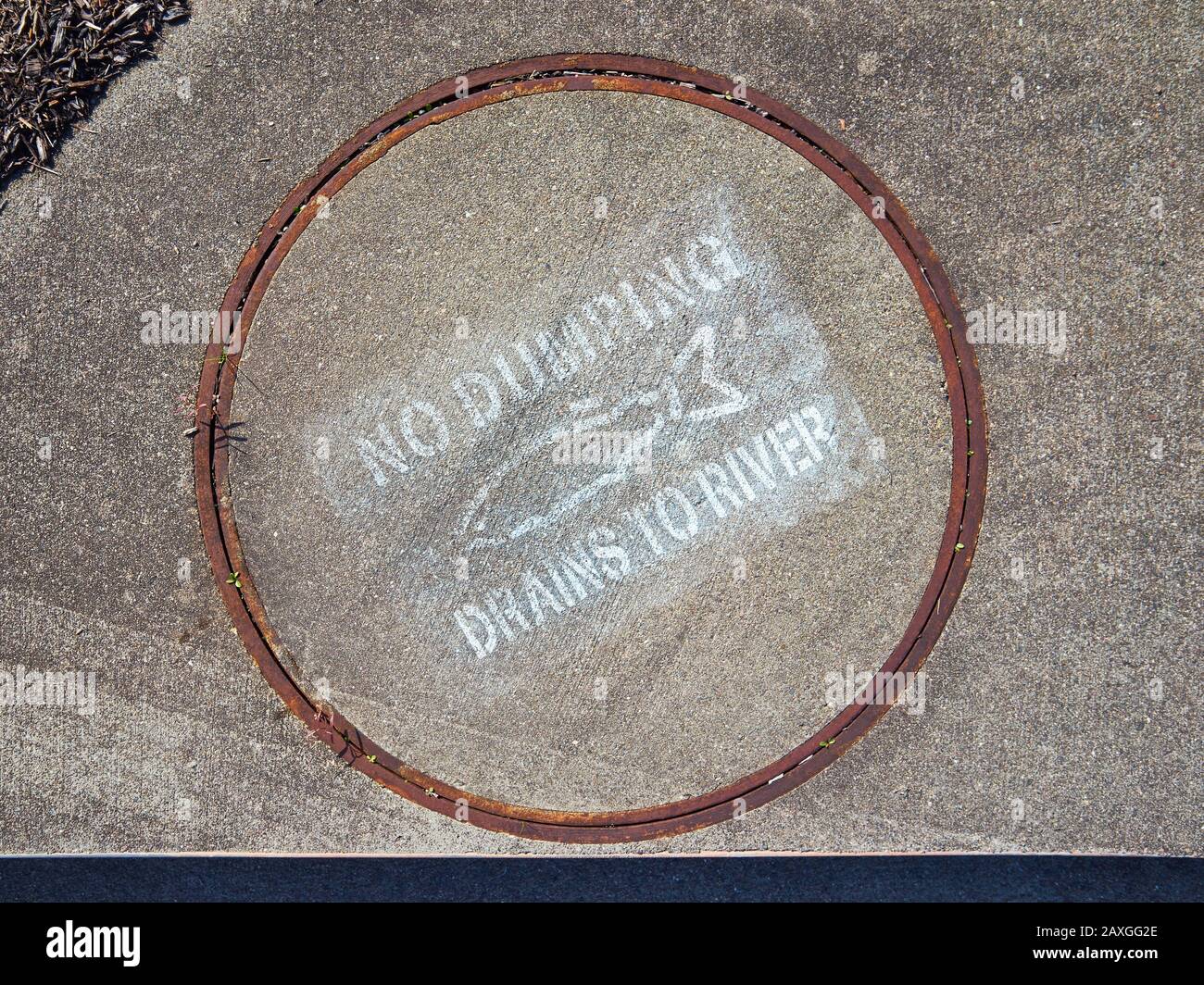 A manhole cover over a drain on the side of a street with a fish picture on it says NO DUMPING DRAINS TO RIVER in Santa Rosa, California. Stock Photo