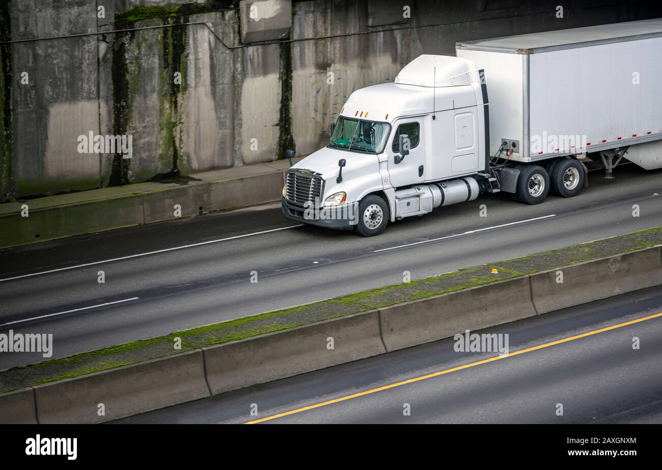 Big rig long haul white semi truck with low cab and spoiler for improve aerodynamics transporting cargo in loaded dry van semi trailer running on the Stock Photo