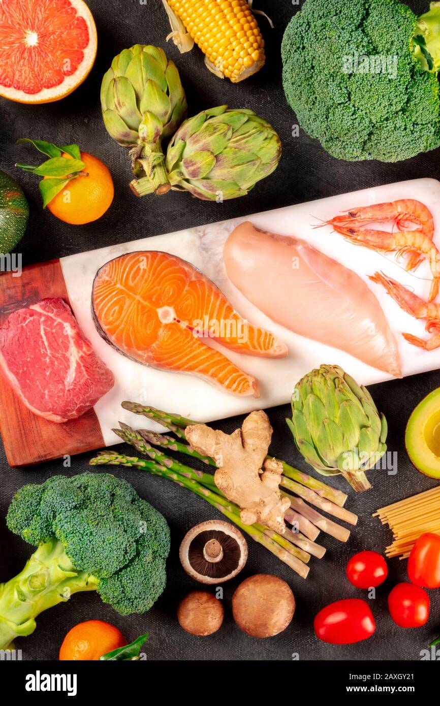 Food flat lay. Meat, fish, poultry and seafood with fruit, vegetables, and mushrooms, shot from the top on a black background Stock Photo