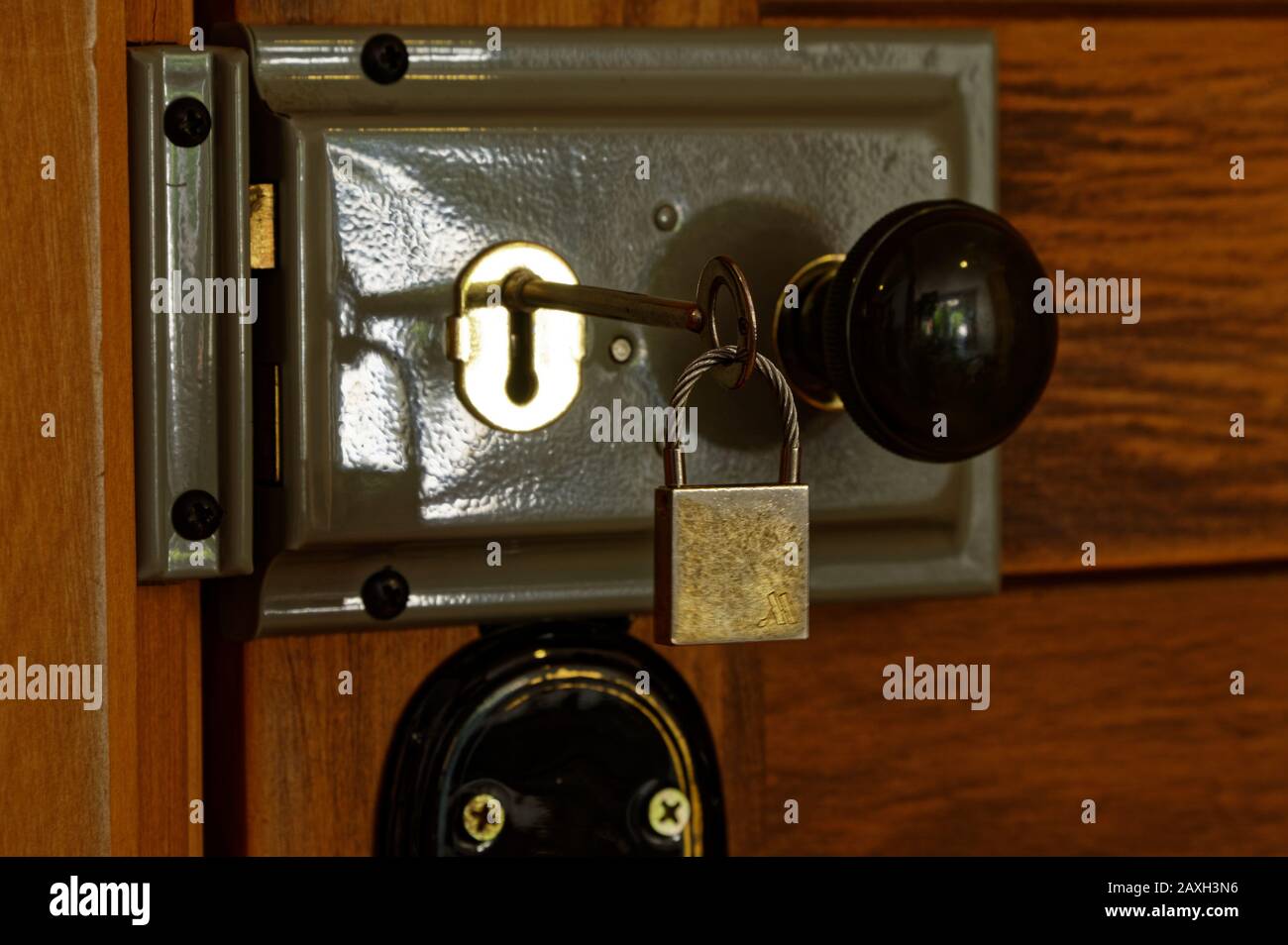 A key with a little padlock on the end of it is inserted in a key hole on a mortise lock on a wooden door Stock Photo