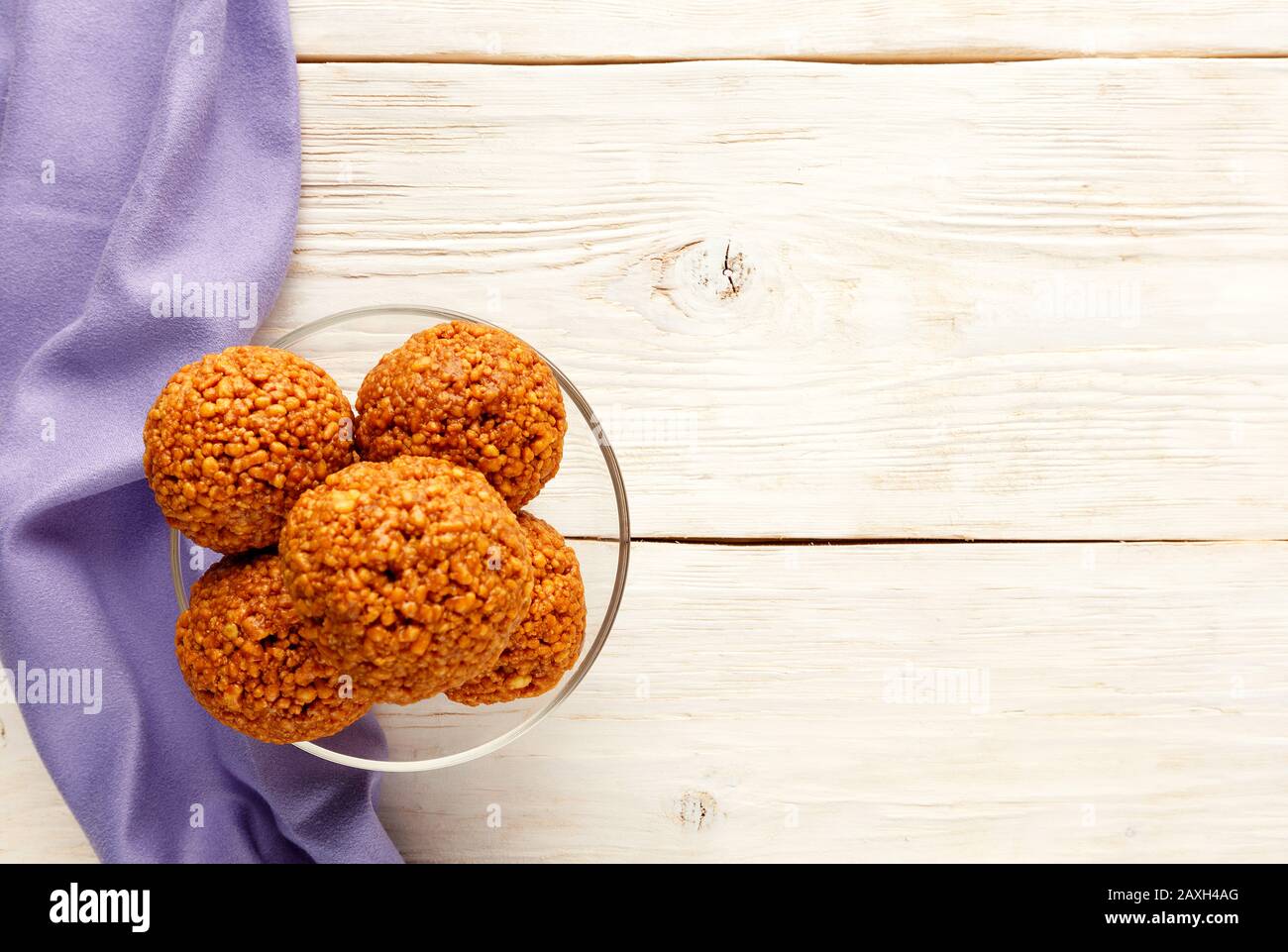 Home energy balls with walnuts, peanuts, honey and banana on a light wooden surface with a purple napkin on the left, top view. Stock Photo