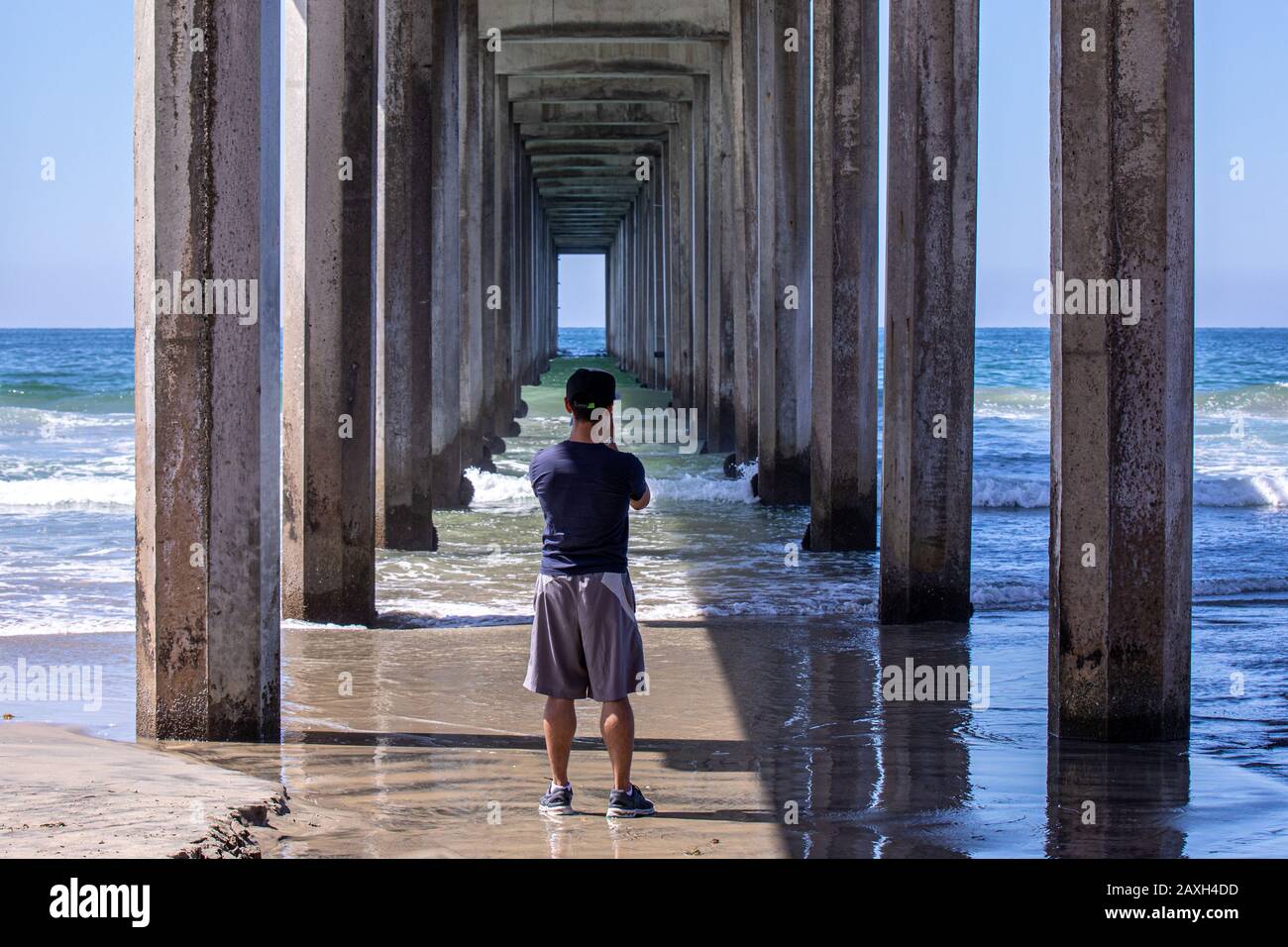 A young man taking pictures of the ocean from under the concrete pier, San Diego, California Stock Photo