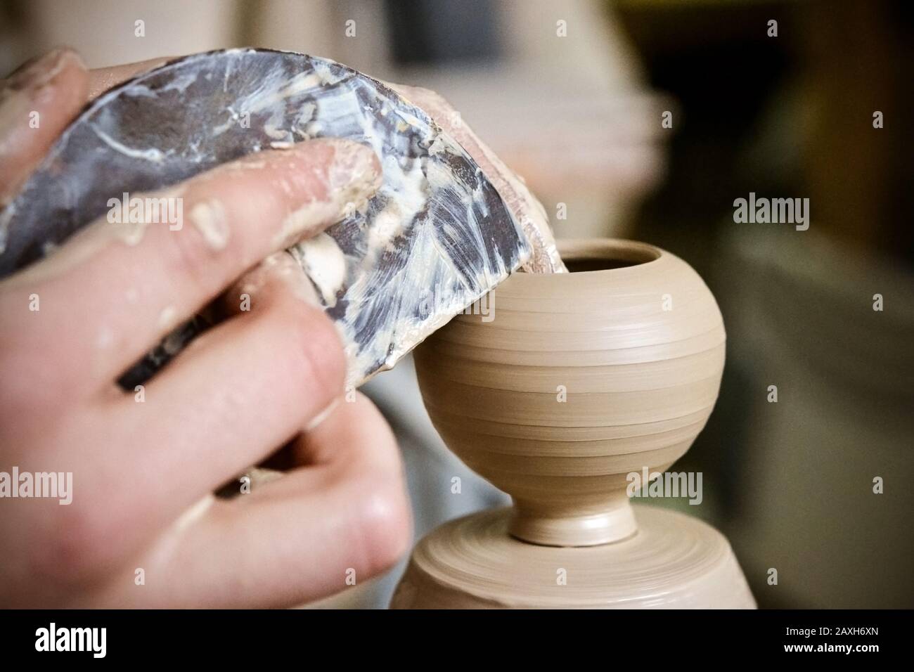 Potter makes a pretty small vase from clay, using the tool for surface leveling close-up macro. Space for text. Stock Photo