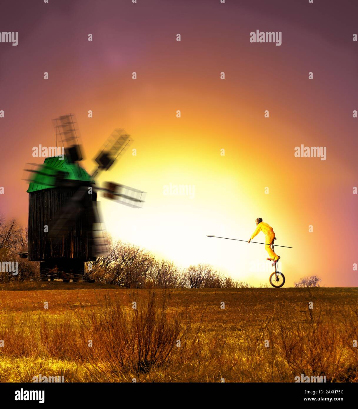 a clown on a unicycle riding with a lance in his hand towards the windmil during sunset. Stock Photo