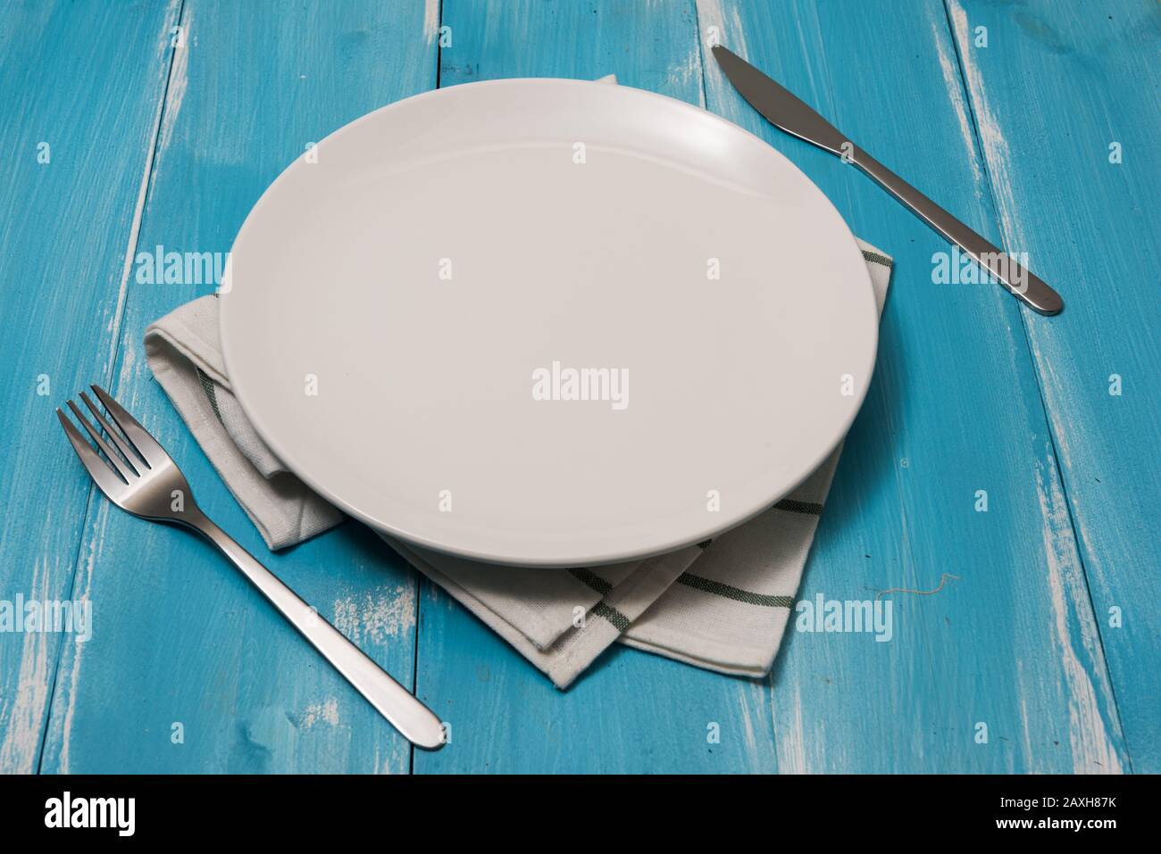 White Round Plate with utensils and dish towel on ocean blue wooden table background with perspective Stock Photo