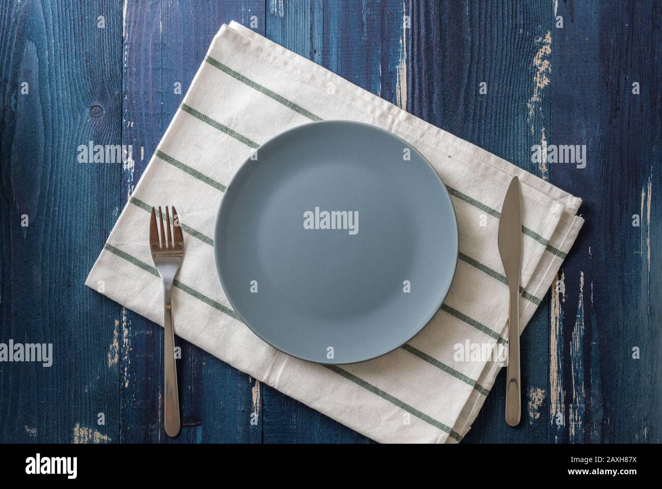 Blue Round Plate with utensils and dish towel on ocean blue wooden table background Stock Photo