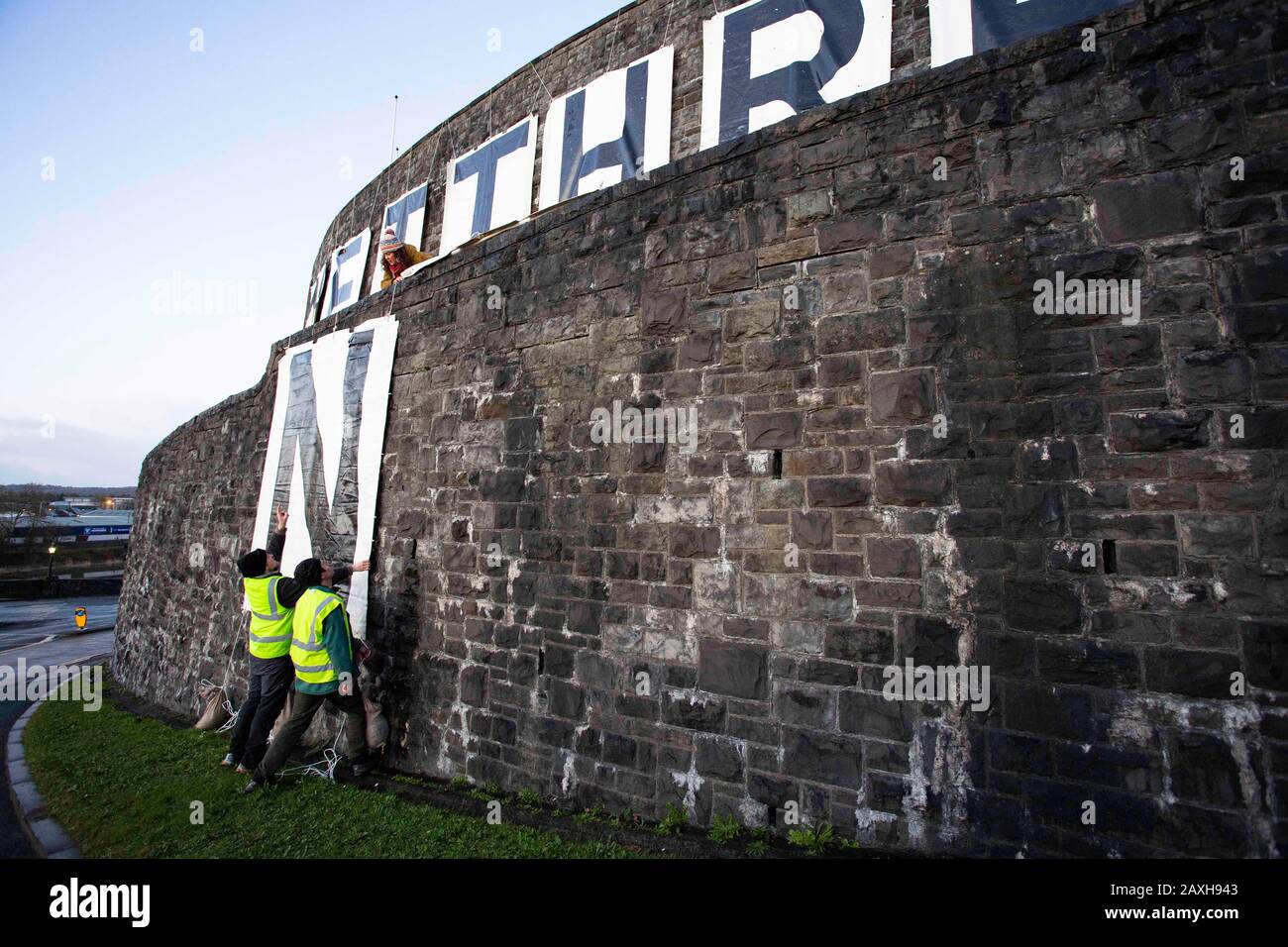Carmarthen, UK. 12 February, 2020. Members of Extinction Rebellion in Carmarthen unfurl banners reading "Act Now" ("Gweithredwch Nawr" in Welsh) on the sides of County Hall in Carmarthen. Credit: Gruffydd Ll. Thomas/Alamy Live News Stock Photo