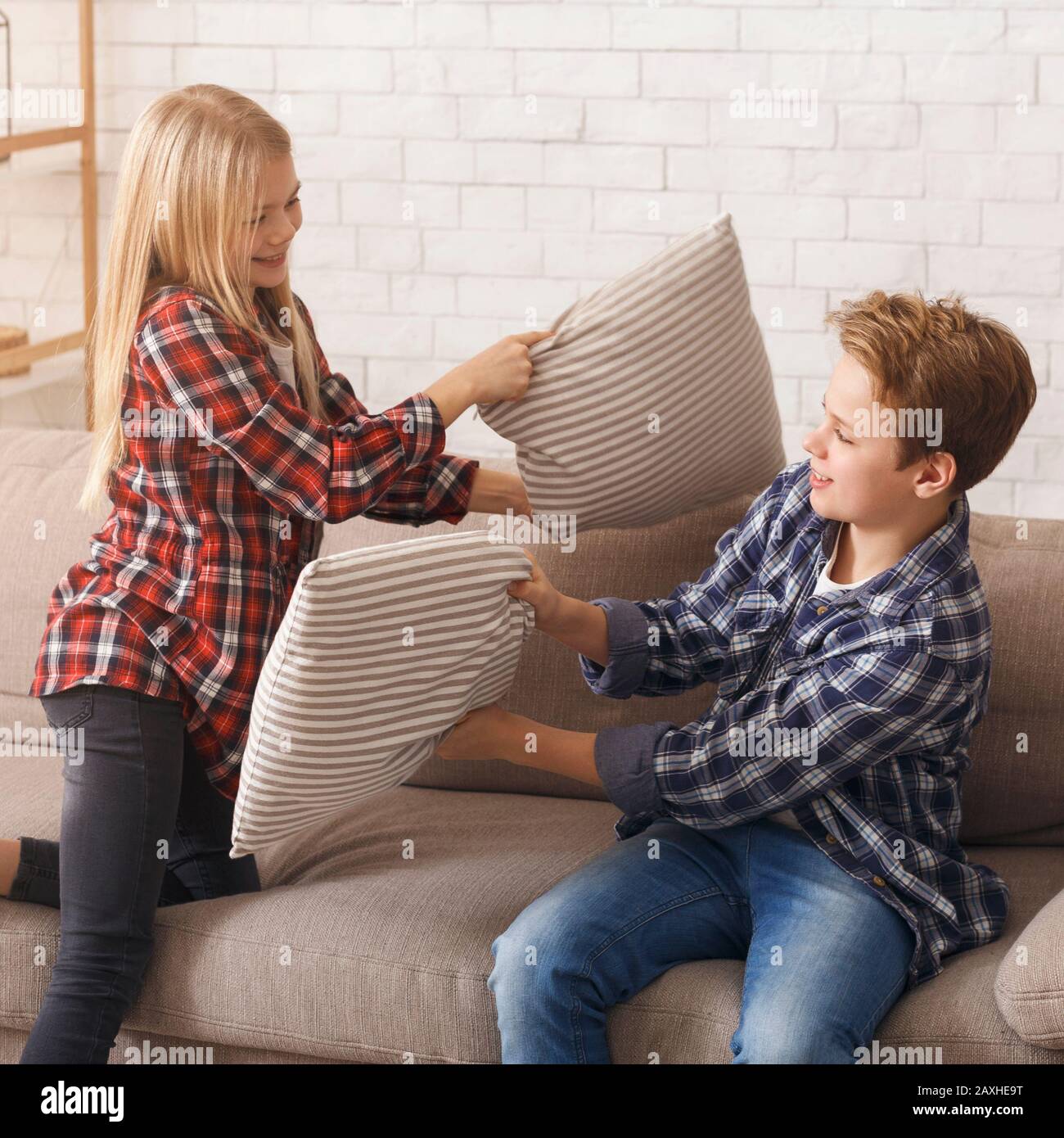 Two Kids Having Pillow Fight Playing On Couch Indoor Stock Photo