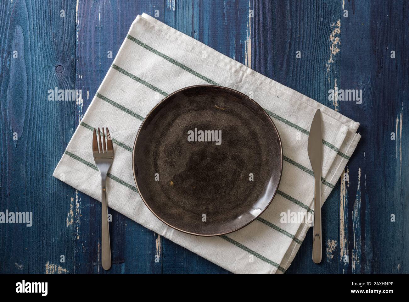 Brown Round Plate with utensils and dish towel on ocean blue wooden table background Stock Photo