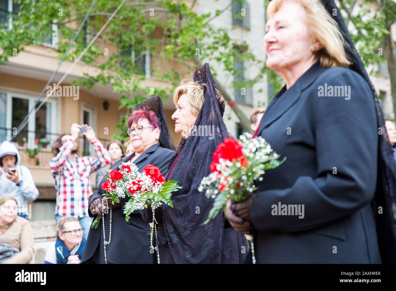 Holy Thursday procession of church brotherhood penitents. Women in black dresses and mantillas standing with flowers in hands Stock Photo
