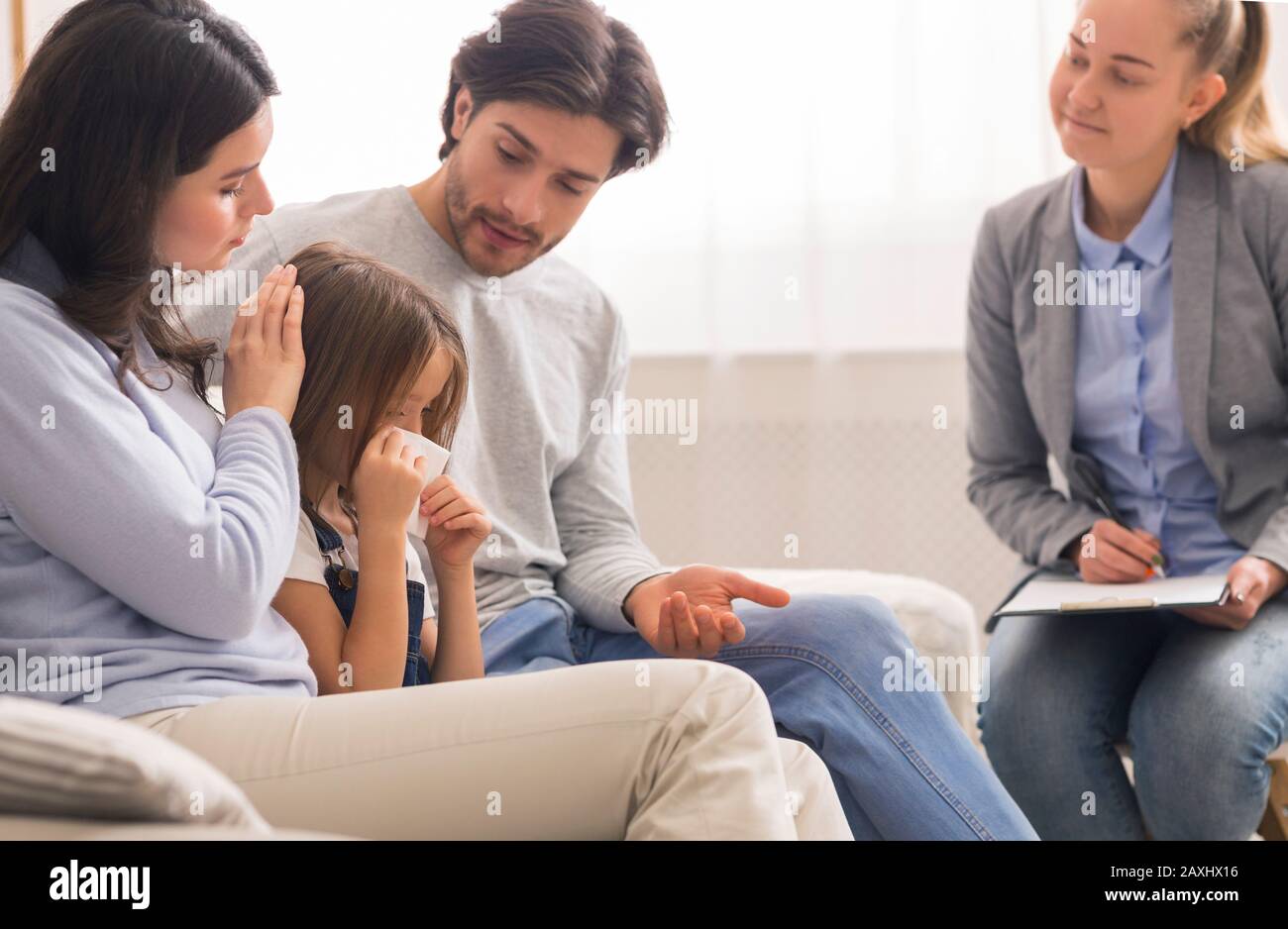 Caring parents comforting their little crying daughter at children psychologist's office Stock Photo