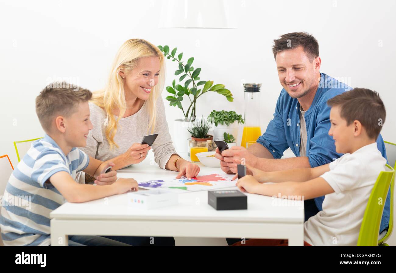Happy young family playing card game at dining table at bright modern home. Stock Photo