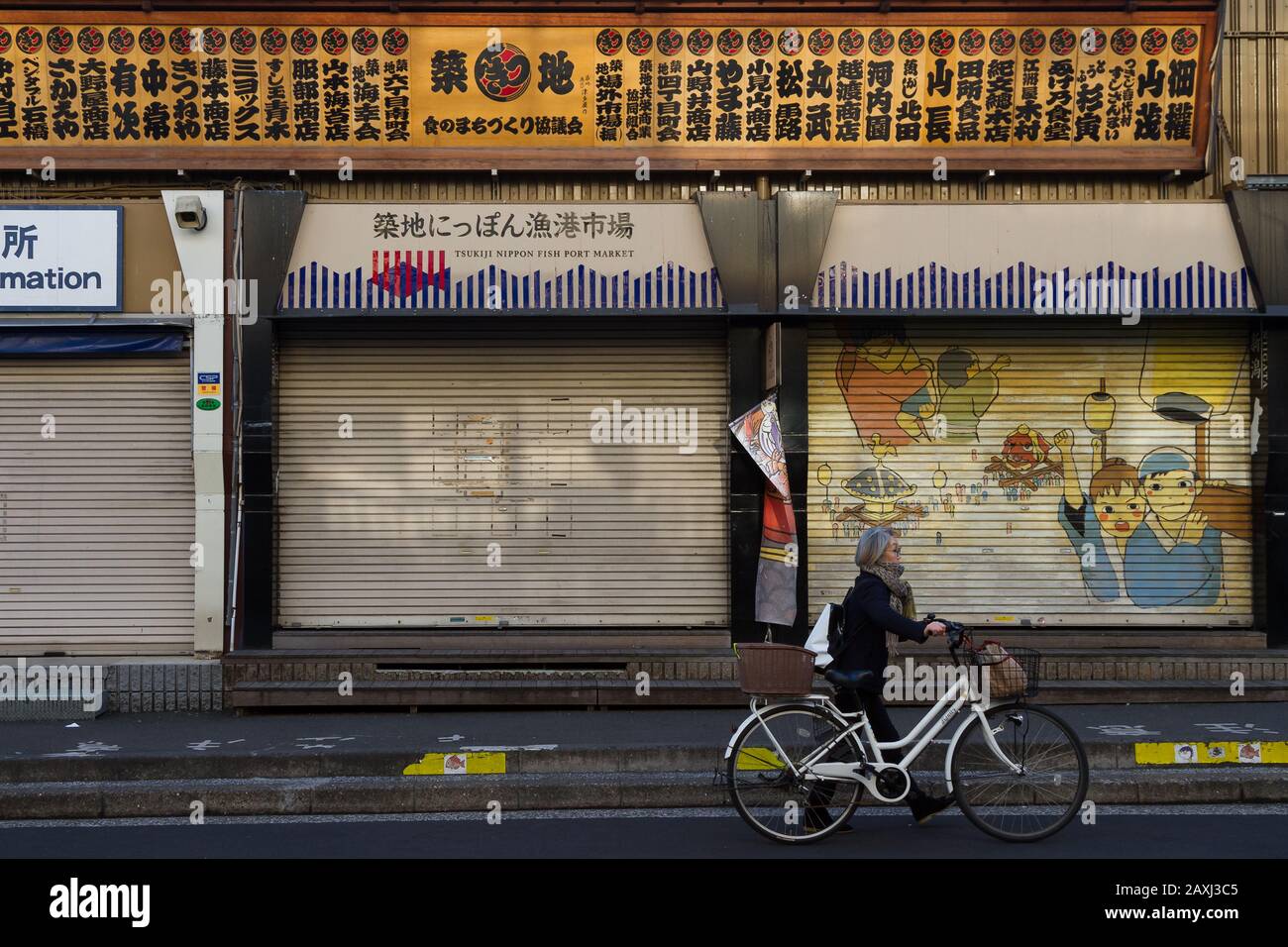 An older Japanese woman pushes a bicycle passed the shuttered store