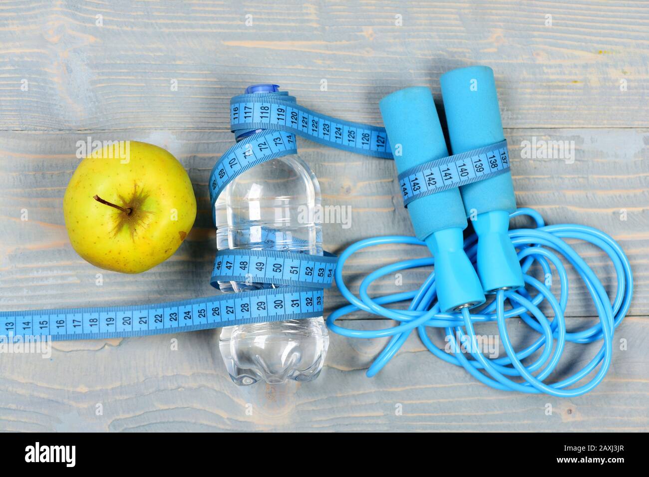 Centimeter tied around sports equipment in cyan blue on wooden vintage  background. Tools for healthy lifestyle. Workout and weight loss concept.  Bottle, apple, measuring tape and jump rope, top view Stock Photo 
