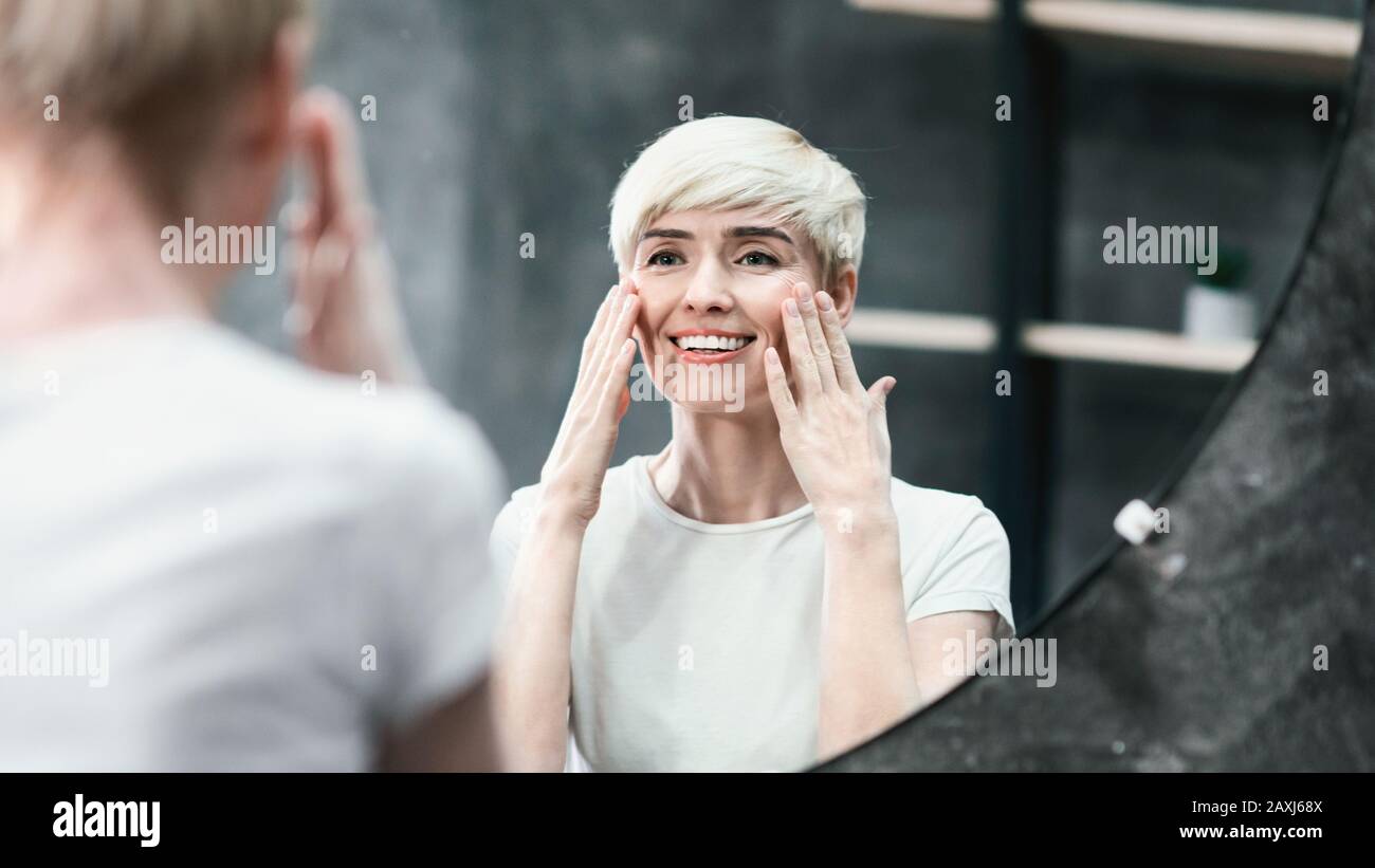 Happy Woman Touching Skin Under Eyes Looking In Mirror, Panorama Stock Photo