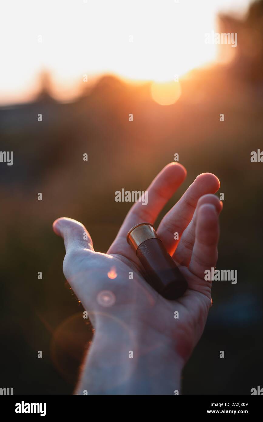 The man is holding a shotgun bullet in the sunlight, sunset. Hunting Concept. Stock Photo