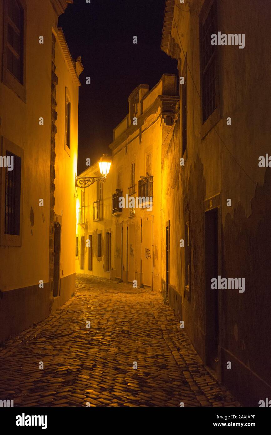 Narrow alleyway illuminated by glow of orange streetlight in the medieval old town, Cidade Velha, city of Faro, Portugal, Europe, Stock Photo