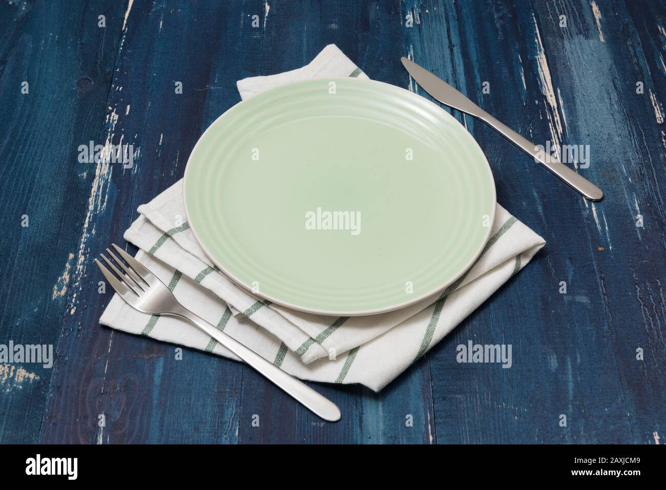 Green Round Plate with utensils and dish towel on ocean blue wooden table background side view Stock Photo