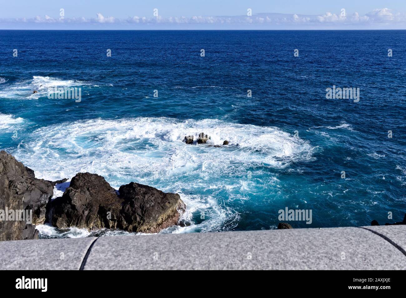 White foam of the waves crashing on the volcanic rock groynes in the ...